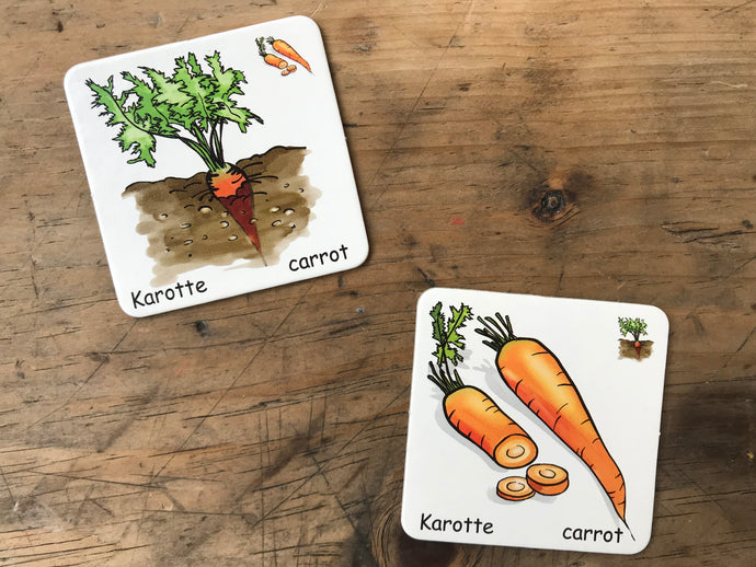 Zwei Memo-Spielkarten mit Karotten-Motiv auf Holztisch – zweisprachig beschriftet auf Deutsch und Englisch